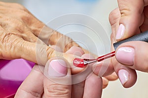 Manicurist applying red varnish to senior woman.