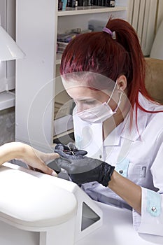 A manicurist in a beauty salon cuts a cuticle in the hands of a client.