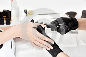 Manicurist in black gloves making manicure using manicure nipper tool.