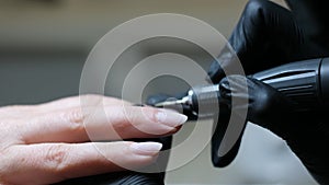 manicurist in black gloves paints nails in beige neutral color close-up beauty salon manicure process with gel polish