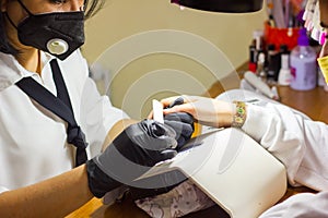 Manicurist with black protective mask work on a woman client hands, Professional works in gloves for sterility photo