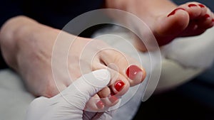The manicurist examines the client's toenails. A female client takes care of red nails. Clean feet