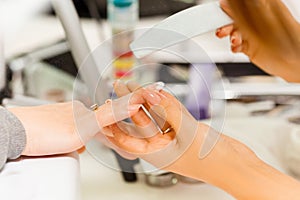 Manicurist makes escalating of nails. Use the nail file makes nail shape. Hands shot close-up on a light background