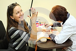 Manicurist makes manicure for woman by nail polish