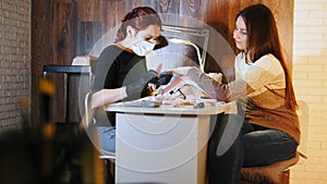Manicurist in medical mask doing manicure for attractive woman in beauty salon