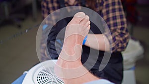 Manicurist removes dry skin from feet of man. She uses electrical hardware machine for russian manicure. Close up view.