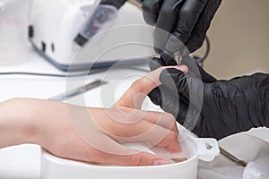 Manicurist removing cuticle from female nails by metal pusher during soaking fingernails in the bath at nail salon