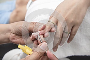 A manicurist uses a nail pusher to scrape off old polish from a fingernail. At a salon or nail spa
