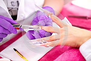 Manicurist wearing purple gloves placing artificial nail enhancements during a manicure treatment