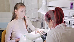 Manicurist woman in a beauty salon decorates client`s nails with gel varnish with rhinestones