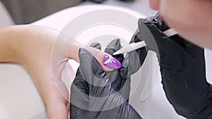 Manicurist woman in a beauty salon decorates client's nails with gel varnish with rhinestones.