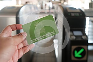 Manila, Philippines: hand holds Light Rail Transit 1 Single Journey Ticket in front of tap machines. Close-up of LRT-1 smart card.
