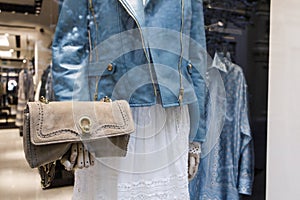 A mannequin in a blue leather jacket holds beige suede clutch bag with gold fittings in a shop window