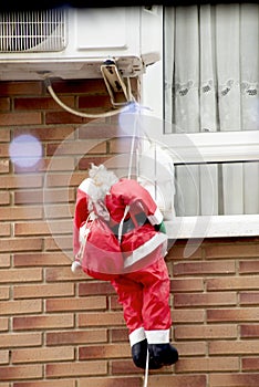 mannequin doll imitation of Santa Claus with a bag on his back climbs a rope to the window of an apartment against the backdrop of