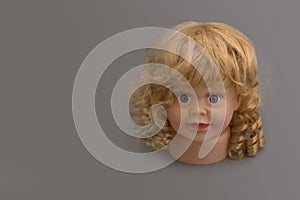 Mannequin head of a little girl looking straight ahead with golden curls on a gray background with coy space. Shop concept, sale,