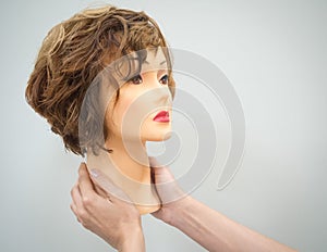 A mannequin head for teaching hairdressing in hands on a light background. Beauty concept.