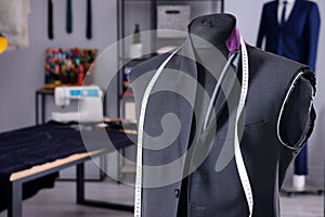 Mannequin with unfinished suit jacket and measuring tape in tailor shop, space for text