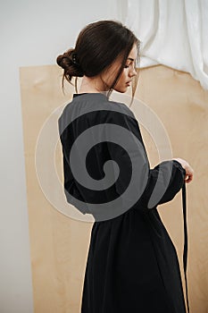 Mannered young beautiful woman tying her dress on a waist. Head in profile.