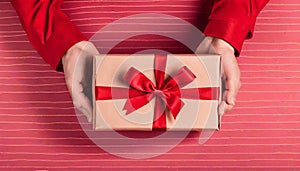 Mano sosteniendo una caja de regalo roja con lazo escarlata sobre fondo carmesÃ­ photo