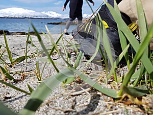 Mans foot resting on warm summer sandy beach with green grass straws and mighty snowy mountain range in the background, northern N