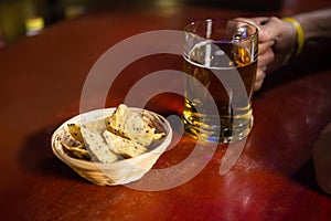 Mans hand holding a mug of beer with snack at counter