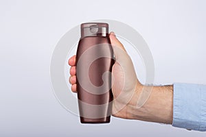 Mans hand holds packaging of shampoo or conditioner on white background. Copy space, mock up