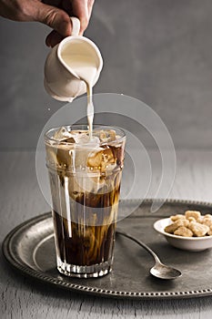 Mans Hand Pours Milk Into Glass of Iced Coffee