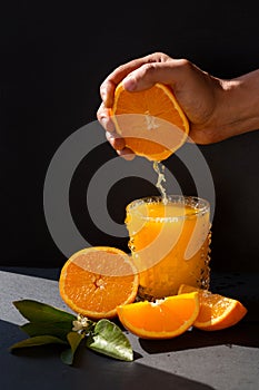 Mans hand sqeezing orange juice into the glass in the bright sunlite