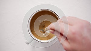 Mans hand stirring coffee with milk in white metal cup on white table