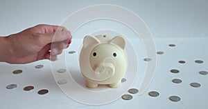 Mans hand throws money into ceramic piggy bank. Piggy bank is associated with frugality and saving even small money for