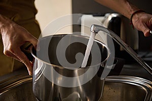 Mans hands filling a stainless steel saucepan with running water until it boils and cooks something. The concept of