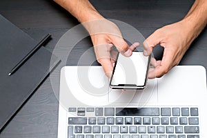 Mans hands typing on smart phone while working on laptop compute