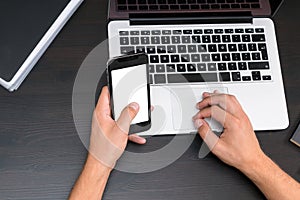 Mans hands typing on smart phone while working on laptop compute