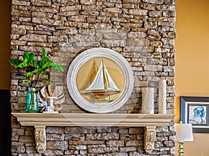 Mantlepiece on rock fireplace decorated with candles, fig leaf in vase and mirror reflecting a model ship