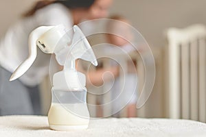 Manual breast pump and bottle with breast milk on the background of mother and baby near the baby`s bed.