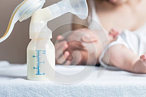 Manual breast pump with milk, mother and baby at background