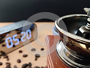 Manual coffee grinder with blurring digital watch and coffee bean at background