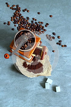 Manual coffee grinder, heap of beans, ground coffee and sugar on a gray concrete background