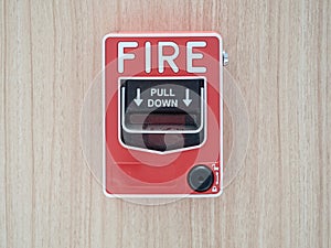 Manual fire alarm activation pull station on modern wooden wall - signage reading: â€œFIRE` and â€œPULL DOWNâ€.