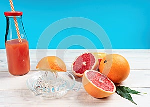 Manual glass citrus fruit juicer and grapefruit juice in a bottle with a straw on a blue background