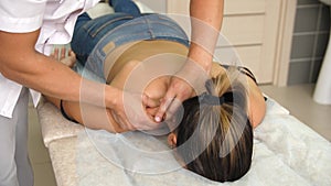 Manual therapist massaging a young woman lying on a massage table, pushing on the back. Male masseur hands massaging