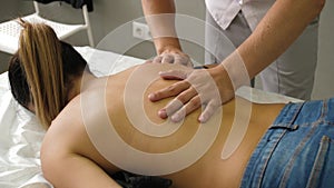 Manual therapist massaging a young woman lying on a massage table, pushing on the back. Young female enjoying
