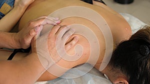 Manual therapist massaging a young woman lying on a massage table, pushing on the back. Young female enjoying