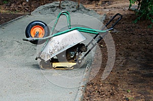 Manual Vibration Plate Compactor is covered with a construction wheelbarrow during rain. Construction site. Use of