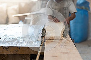 Manual wood concept. Photo of garage or workroom with focus on wood plank on table with blurred unrecognizable cabinetmaker