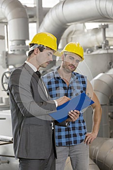 Manual worker with supervisor discussing over clipboard in industry