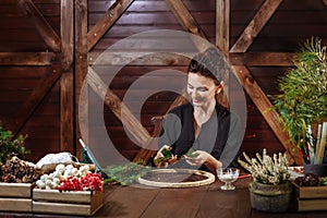 Young Cute smiling Woman designer preparing Christmas Evergreen Tree Wreath. Manufacturer of Christmas decor with their