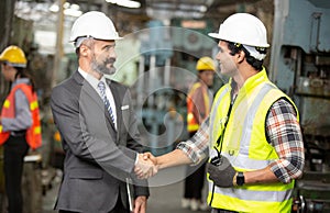 Manufacturing staff engineer in production factory hand shaking with businessman