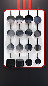 Many aluminum metal new modern cooking pans hang on the wall in the kitchen. Household goods, dishes, kitchen utensils. Storefront