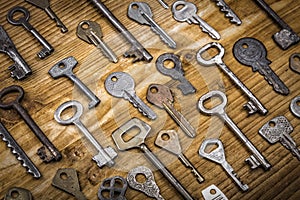 Many assorted old multi-colored metal antique vintage keys of different shapes on wooden scratched table background. Home security